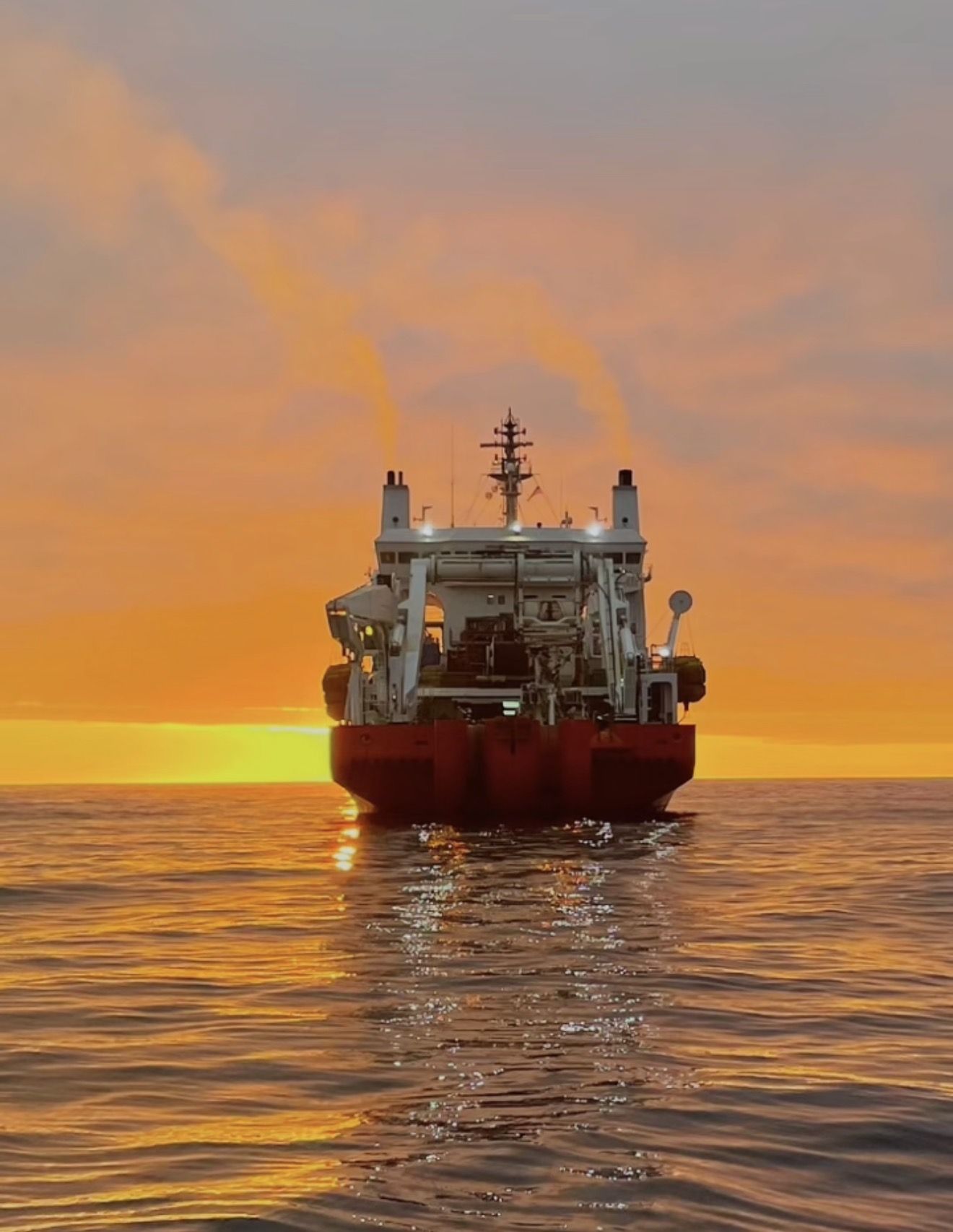 Submarine cable ship holding station offshore at sunset